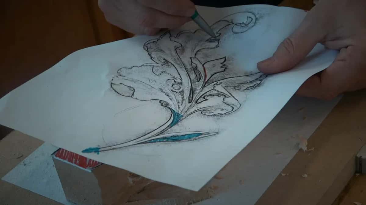 Hands hold up the leaf drawing while a pen tip touches a small part near the top
