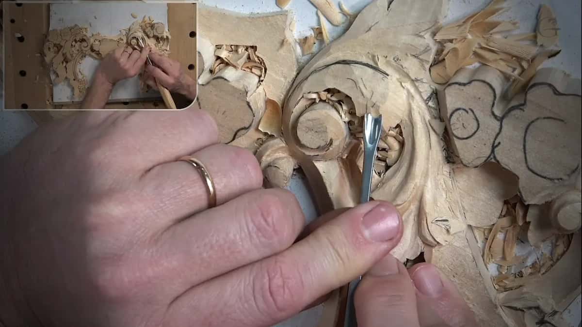 Fingers curled around a small gouge in the leaf beside the scroll, curls of wood all around