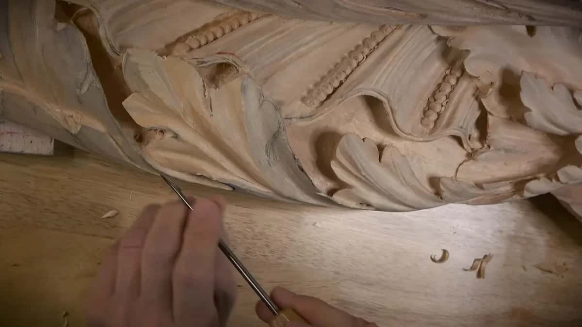 Along the frieze Two hands guiding a long thin blade along the bottom edge of a frieze that carries a bead molding