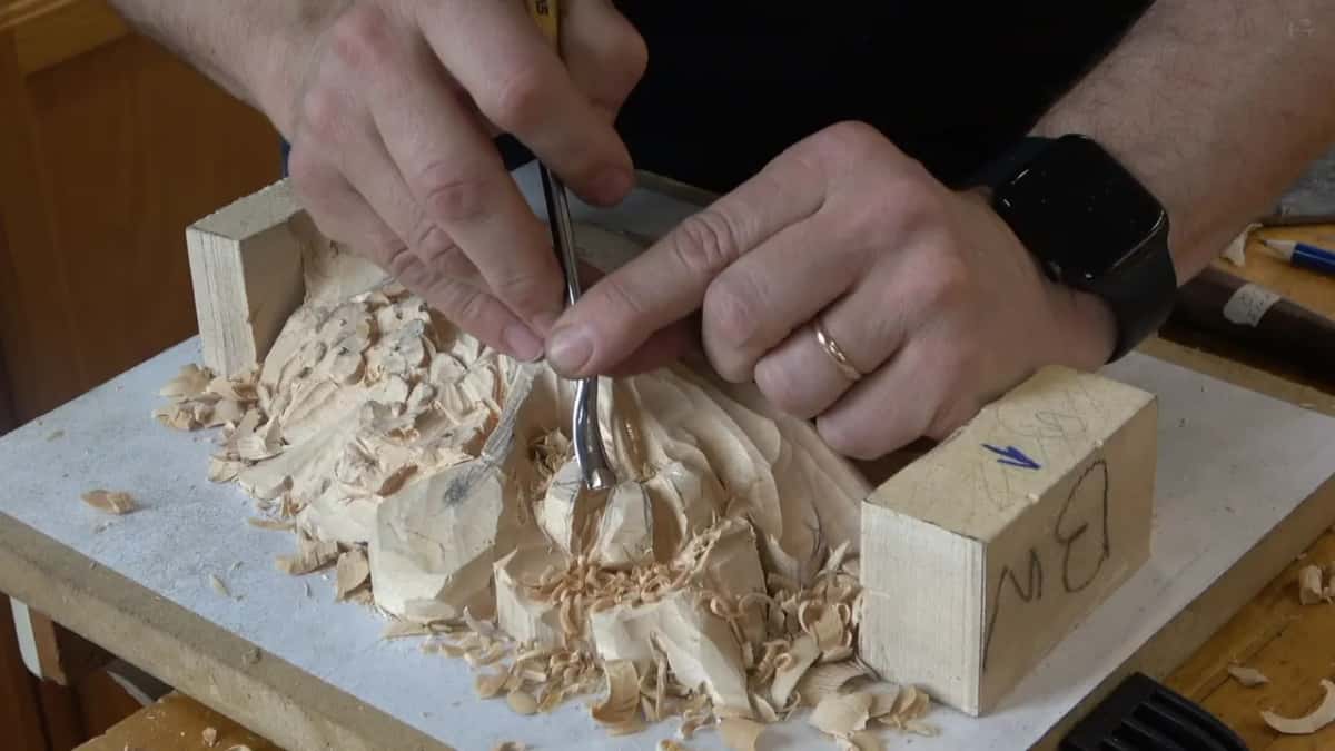 A bent tool gripped in both hands and reaching down between the carved shapes near the end block