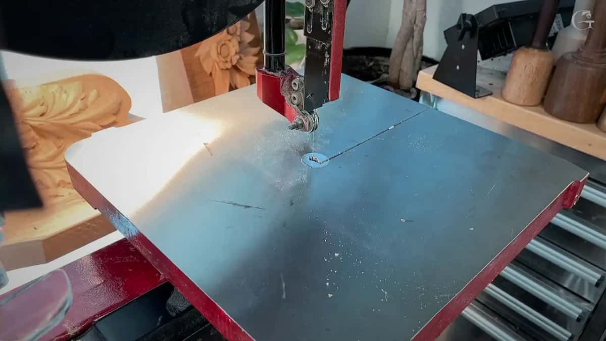 Empty steel band saw table, the blade standing in fine dust under its guide