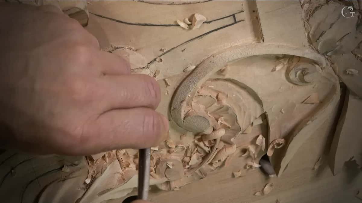 Slim tool held upright in a hollow full of curled chips beside the scroll