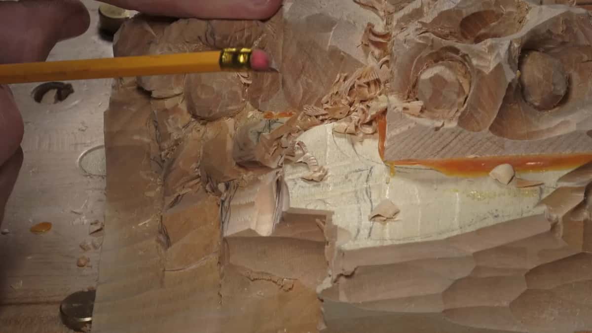 A yellow pencil held flat against the carved wood to test for a straight line