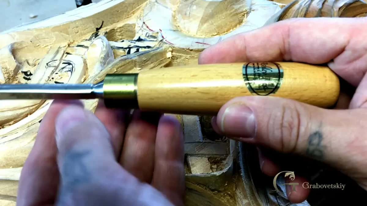 Brass ferrule and round pale handle, held over rough carving