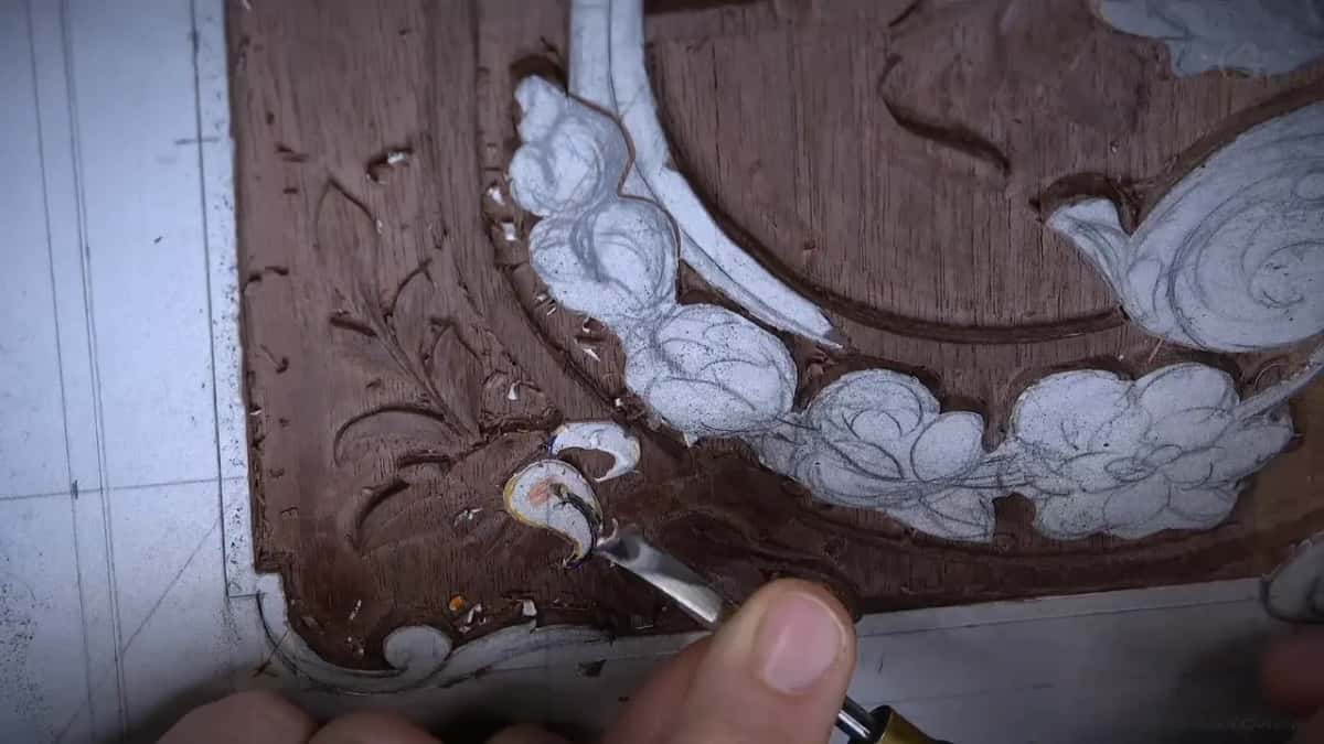 Gouge tip touching a small white curl with a pinkish center, low in the corner of the panel