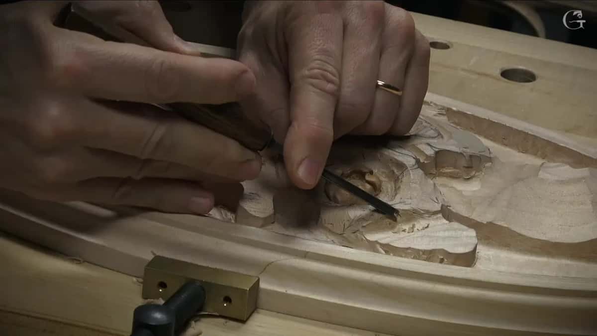 Seen low from the side, hands work a small tool along a petal by the rim
