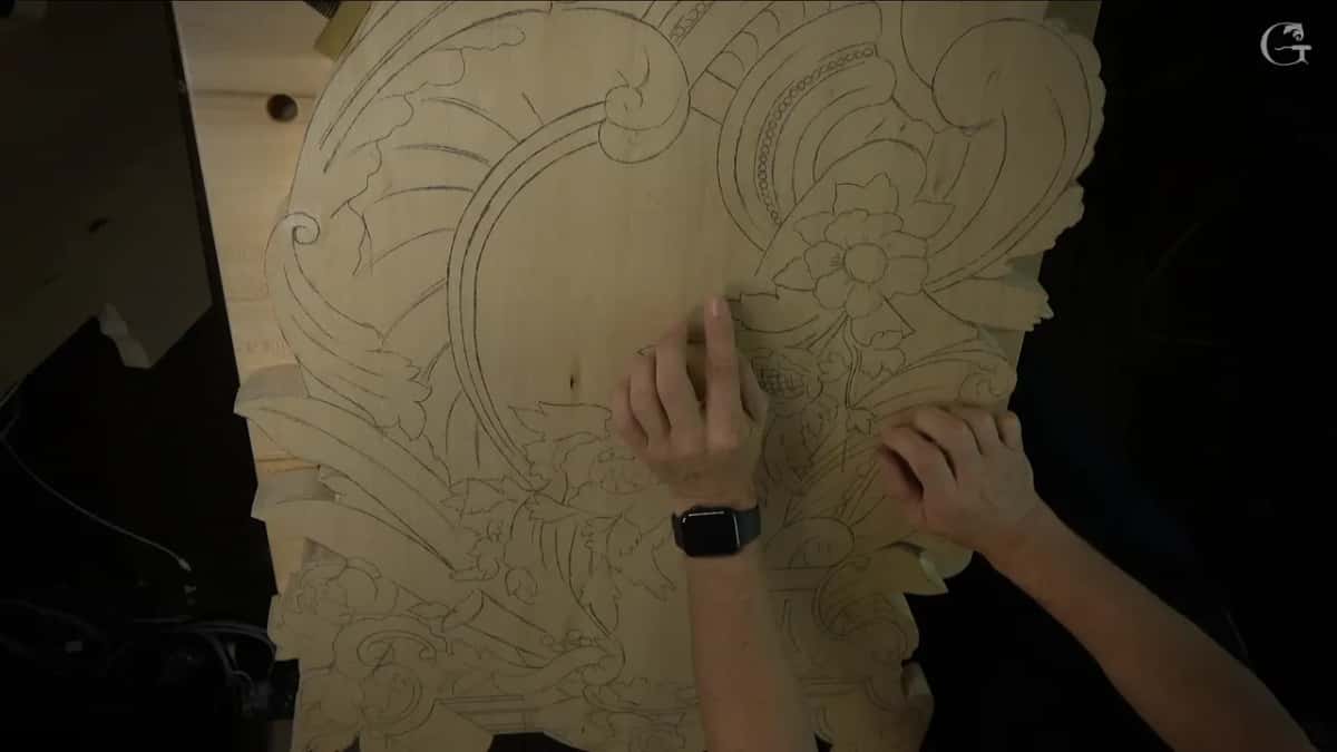 Drawn scrolls, leaves and a flower cover a sawn board, and two hands press flat against the pattern