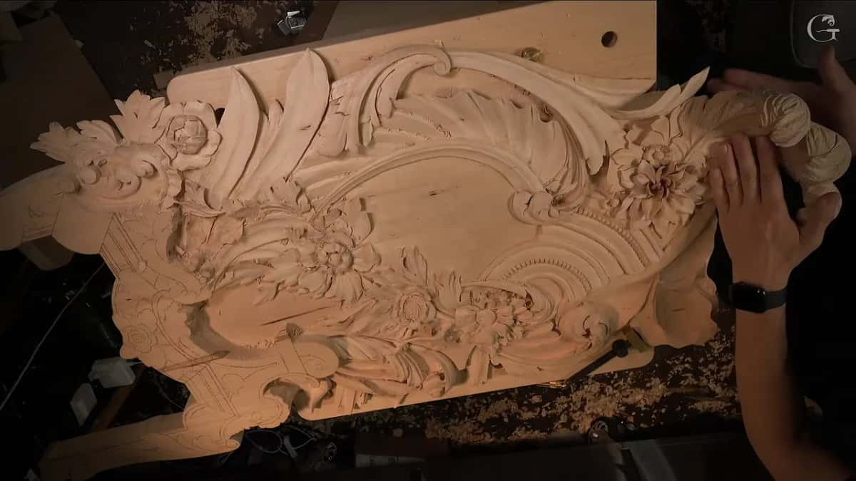 Both hands rest on a big carved panel thick with acanthus leaves and open flowers