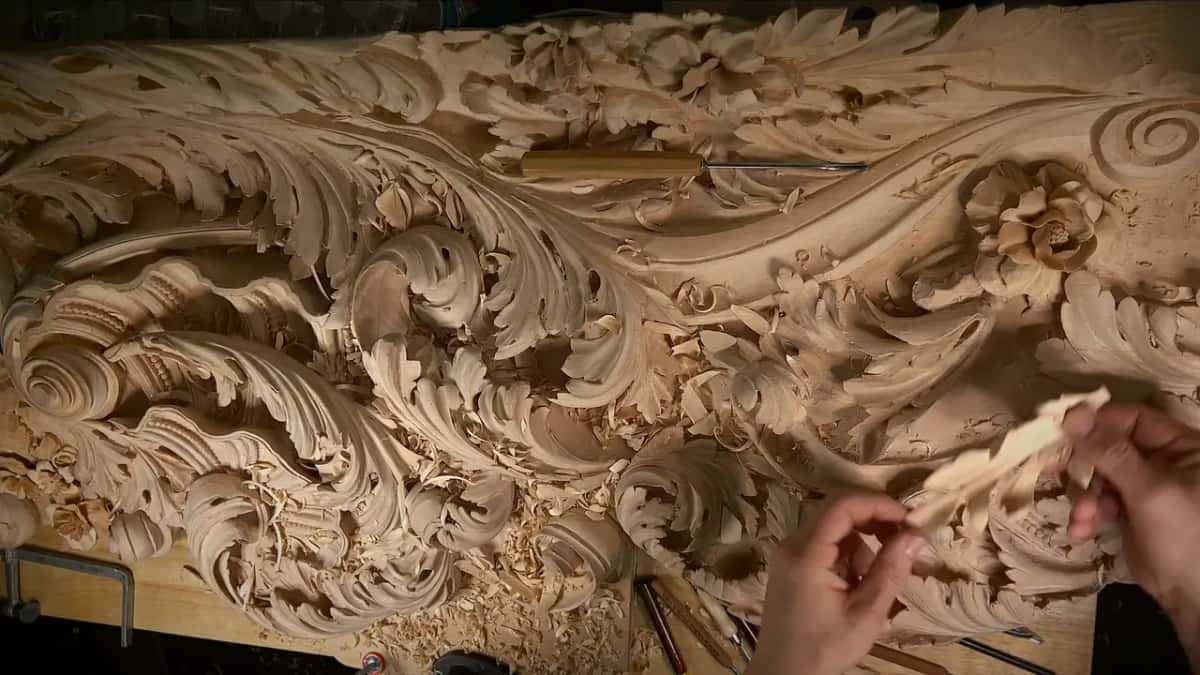 Held over a long carved acanthus panel, a small piece of wood between the fingers