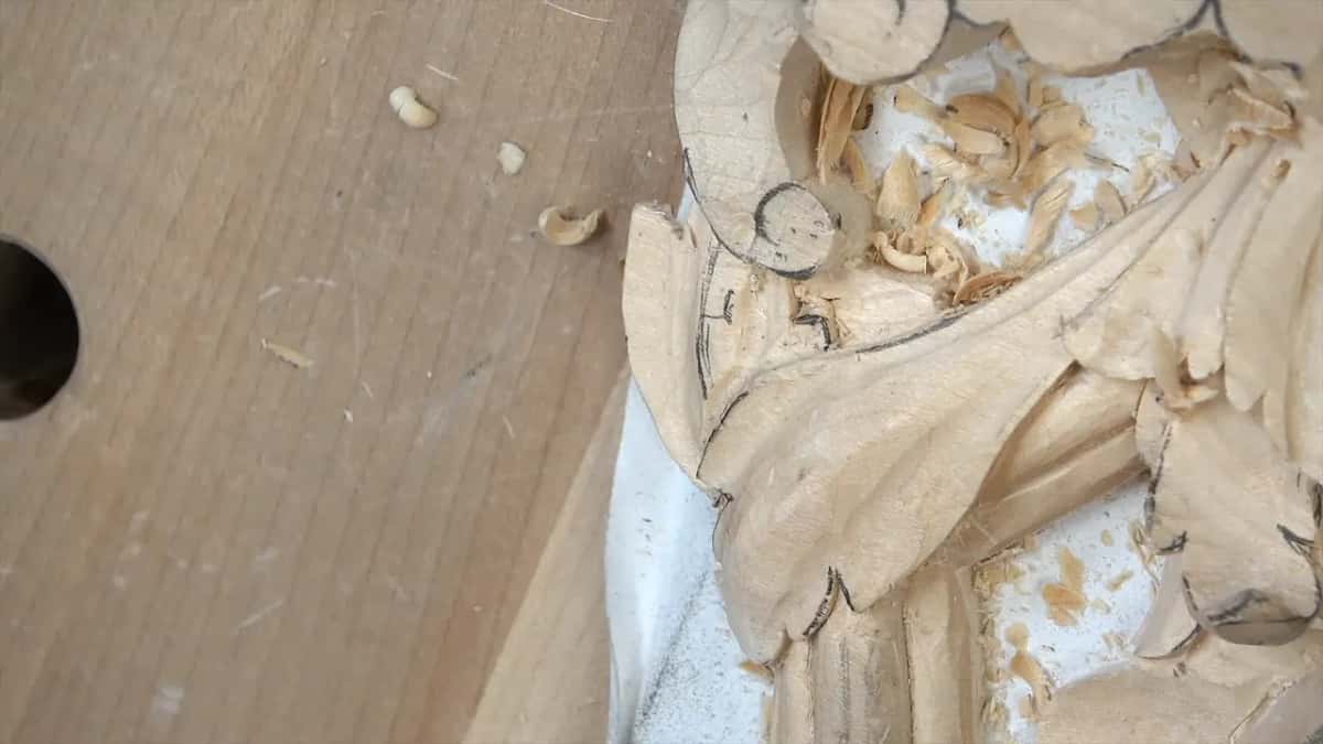 A carved leaf with no tool in view, pencil marks along its edge and shavings above