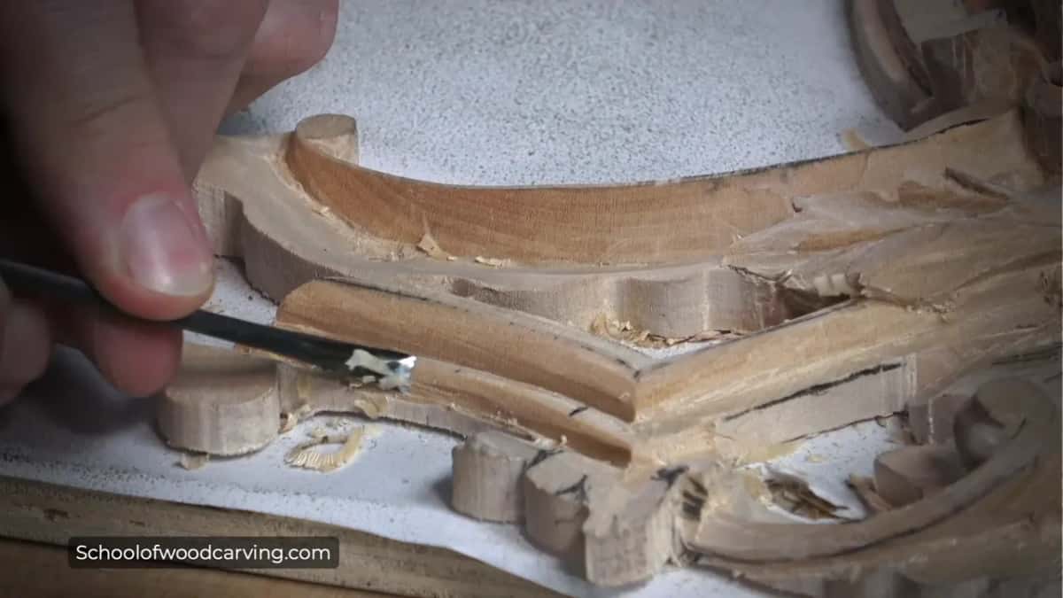 Low side view of the mitered molding, rounded now, a dark bent tool in his fingers at the side