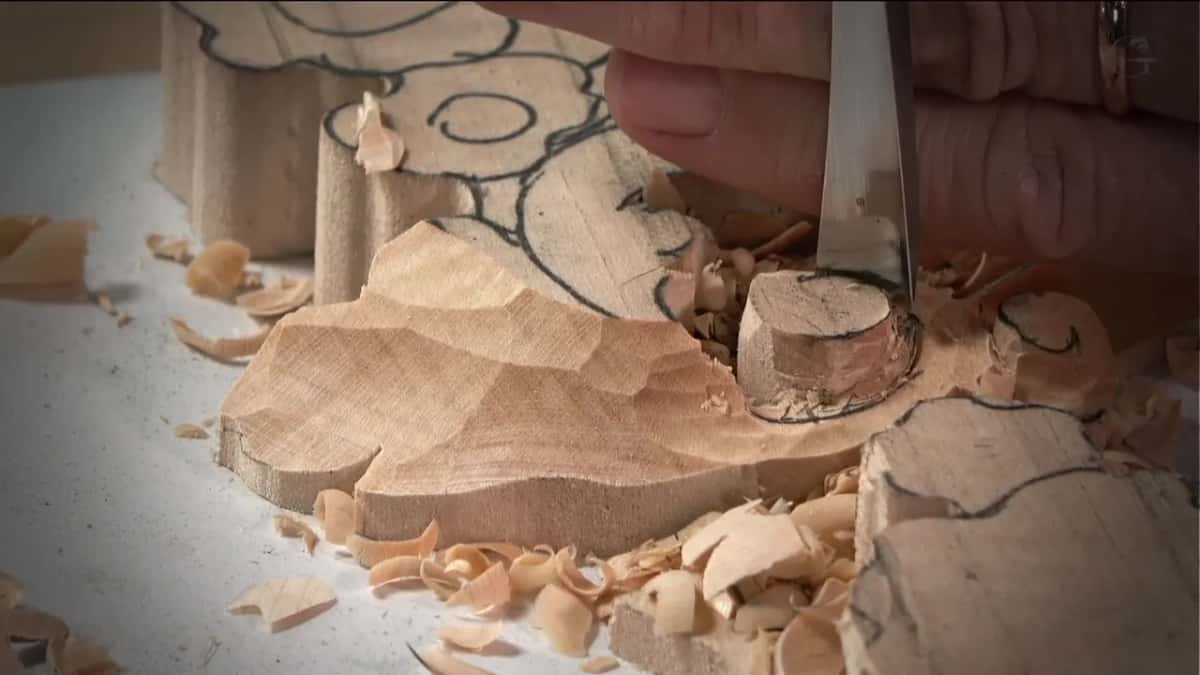 A gouge pressed straight down beside a round stub, curled shavings piled around it