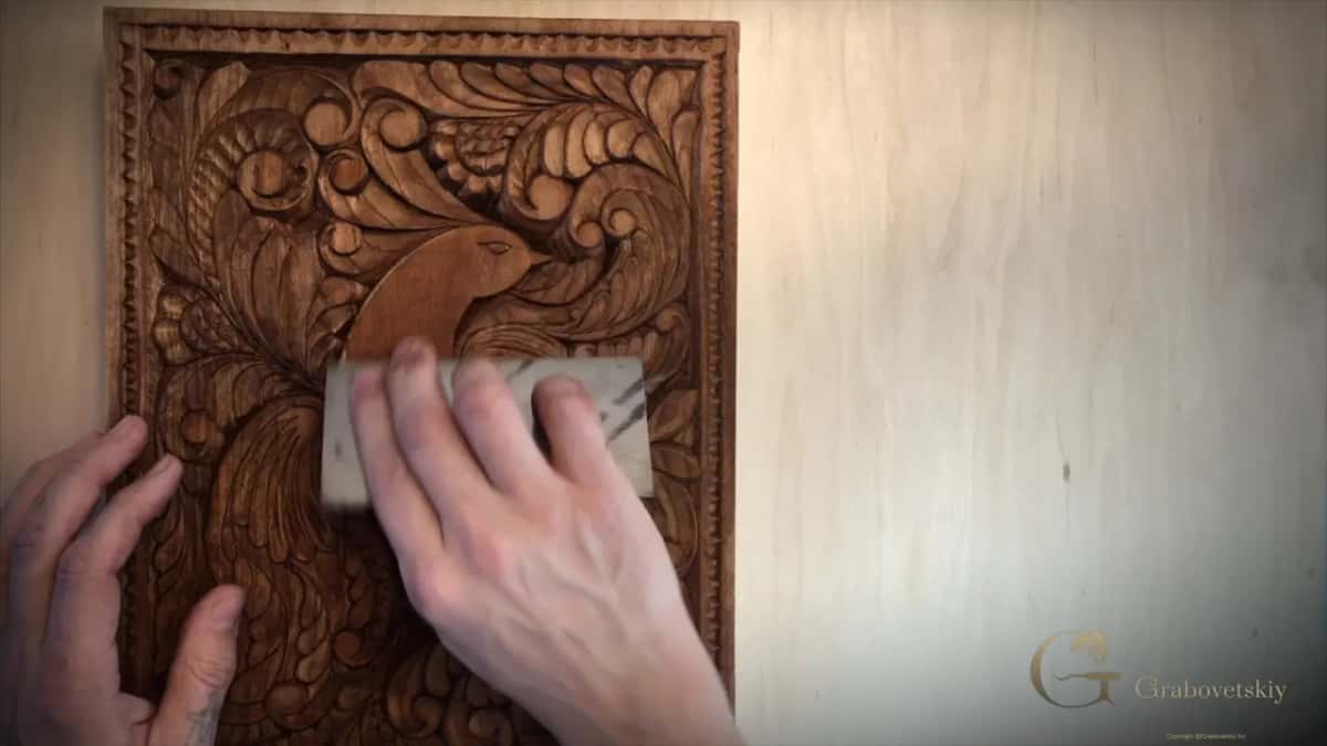 Two hands hold a flat scraper across the stained bird, one at each end