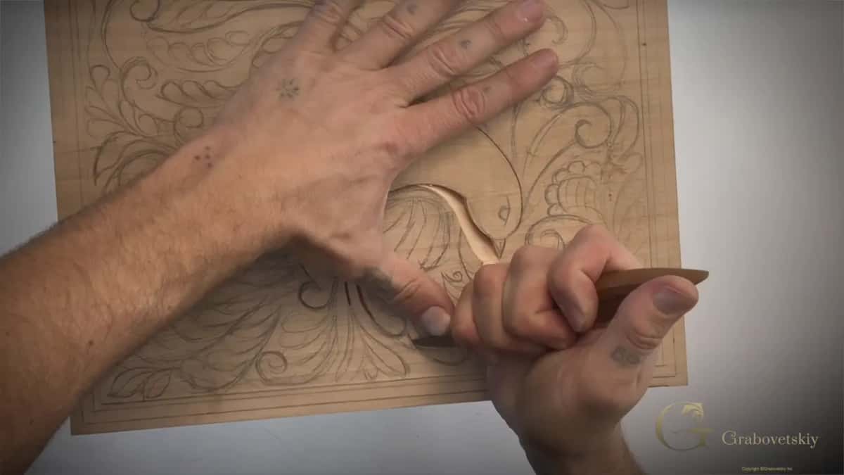 Two hands on the board, the left one pressing flat while the right draws the knife along the head