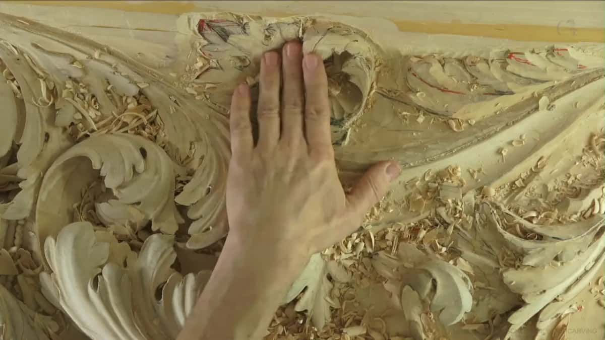 Brought close, a flat hand lies over the carved leaves