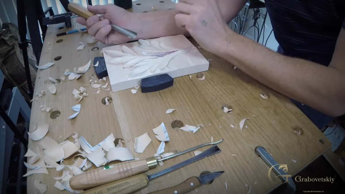 Arm reaching across the bench to the leaf panel, tools and chips in front