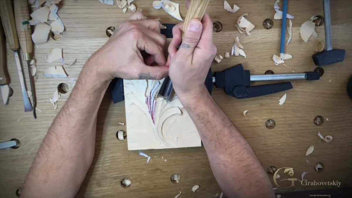 From above, both hands closed together on one gouge at the leaf, the black clamp just beyond them