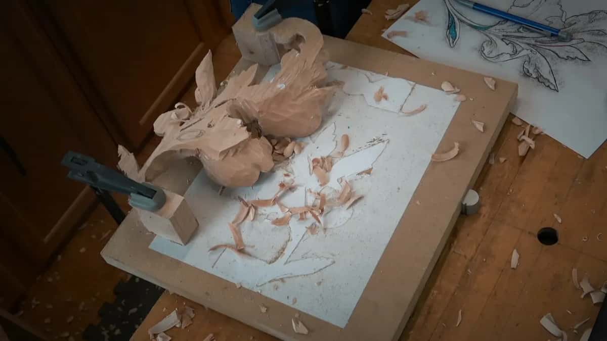 Leaf held down at one end on paper over a board, chips scattered, the design drawing beside it