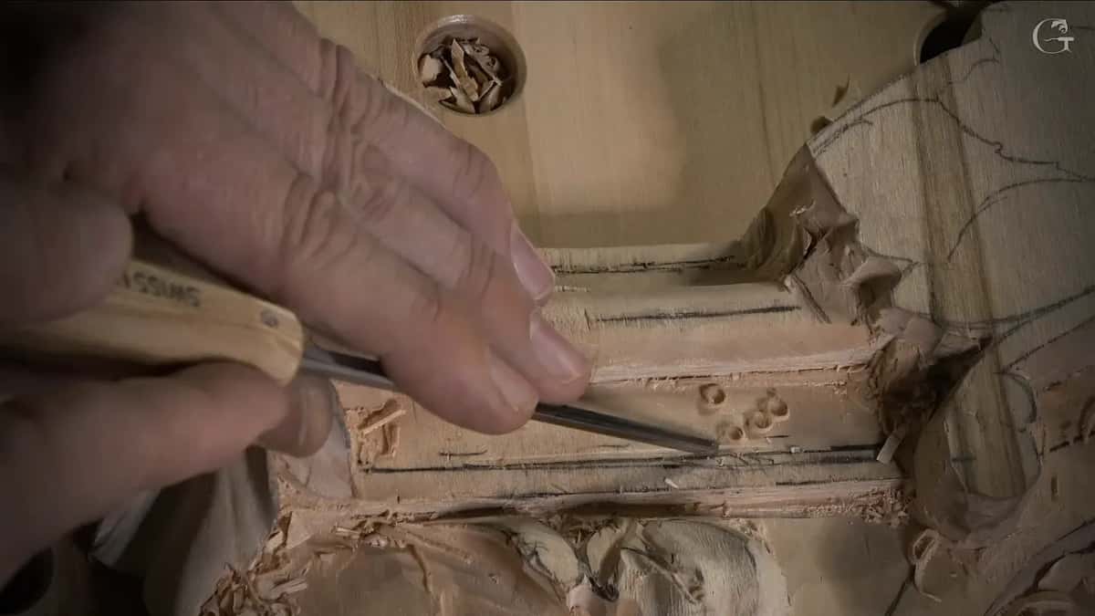 Close up from the side, a narrow tool pushed along a molding groove with small round chips on the band