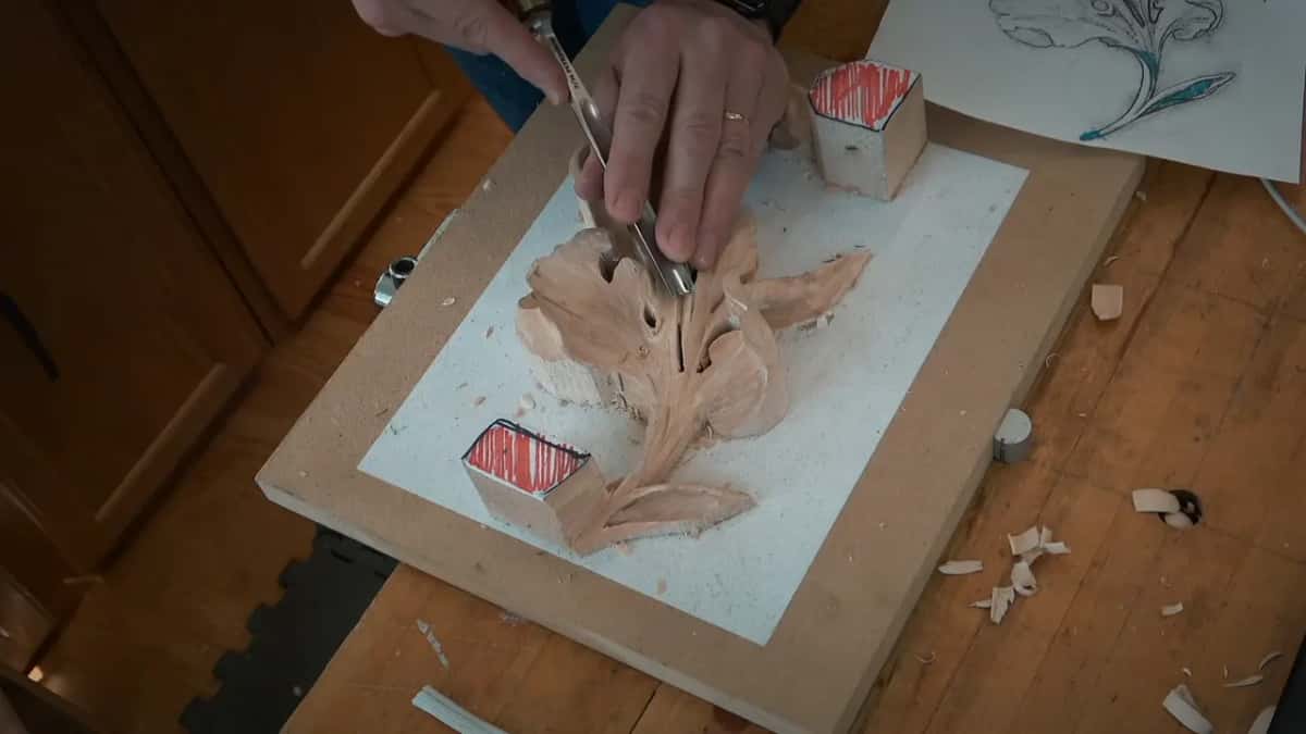 Fingers pinch the tool in the middle of the leaf while the drawing waits at the top of the board