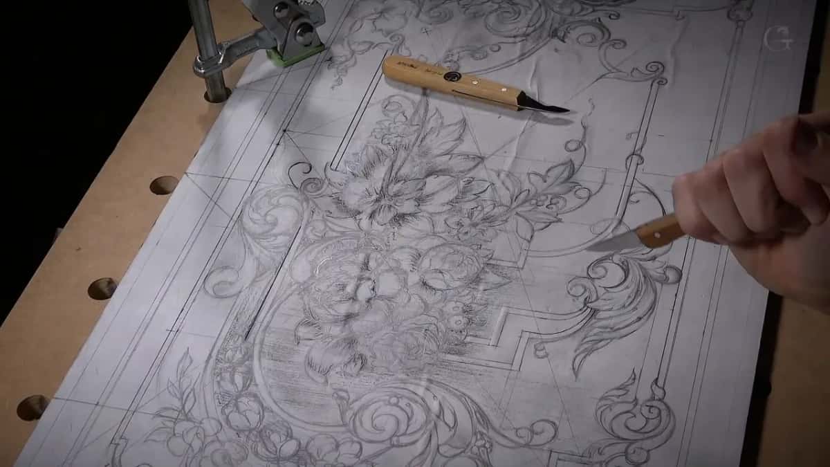 The whole panel drawing sits clamped to the bench, and a carving knife lies near its top edge.