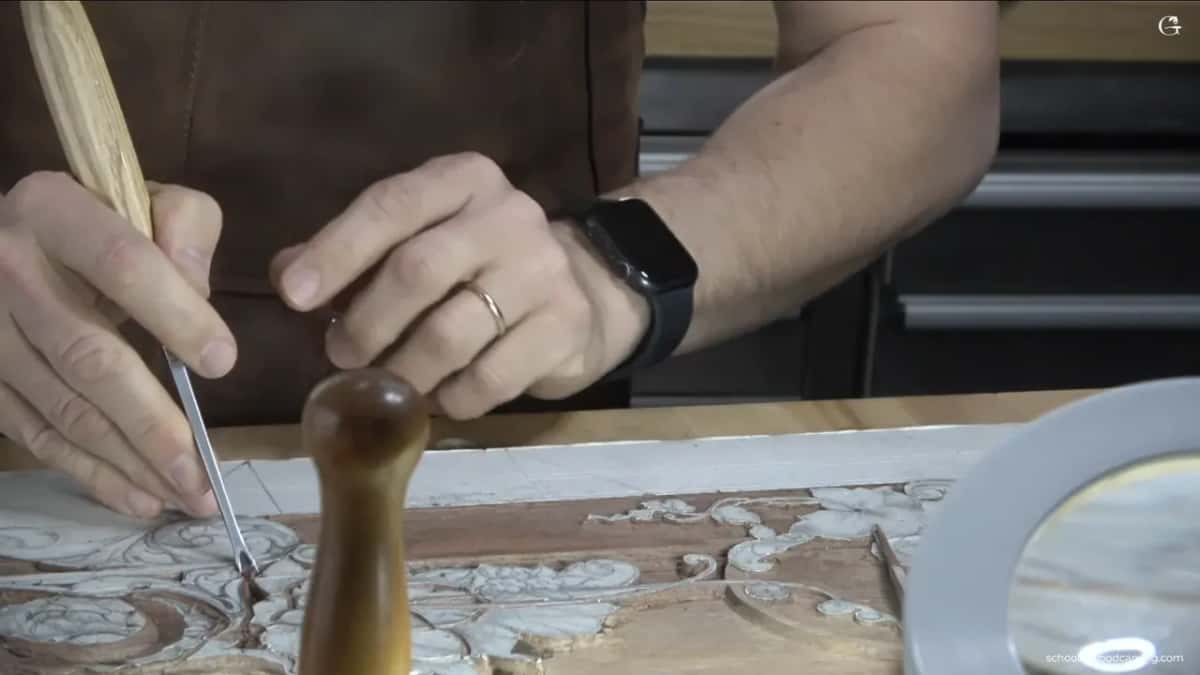 Gouge held down in the carving with a turned mallet standing on the panel in front of it
