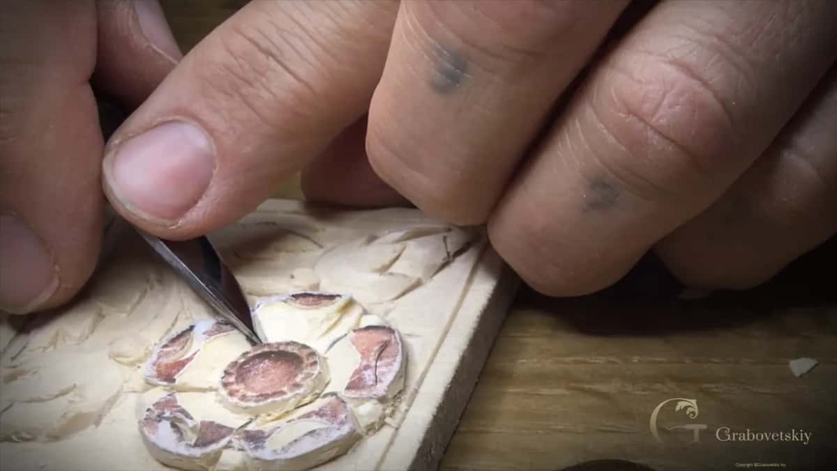 Knife tip between two petals of the flower while the other hand holds the block flat.