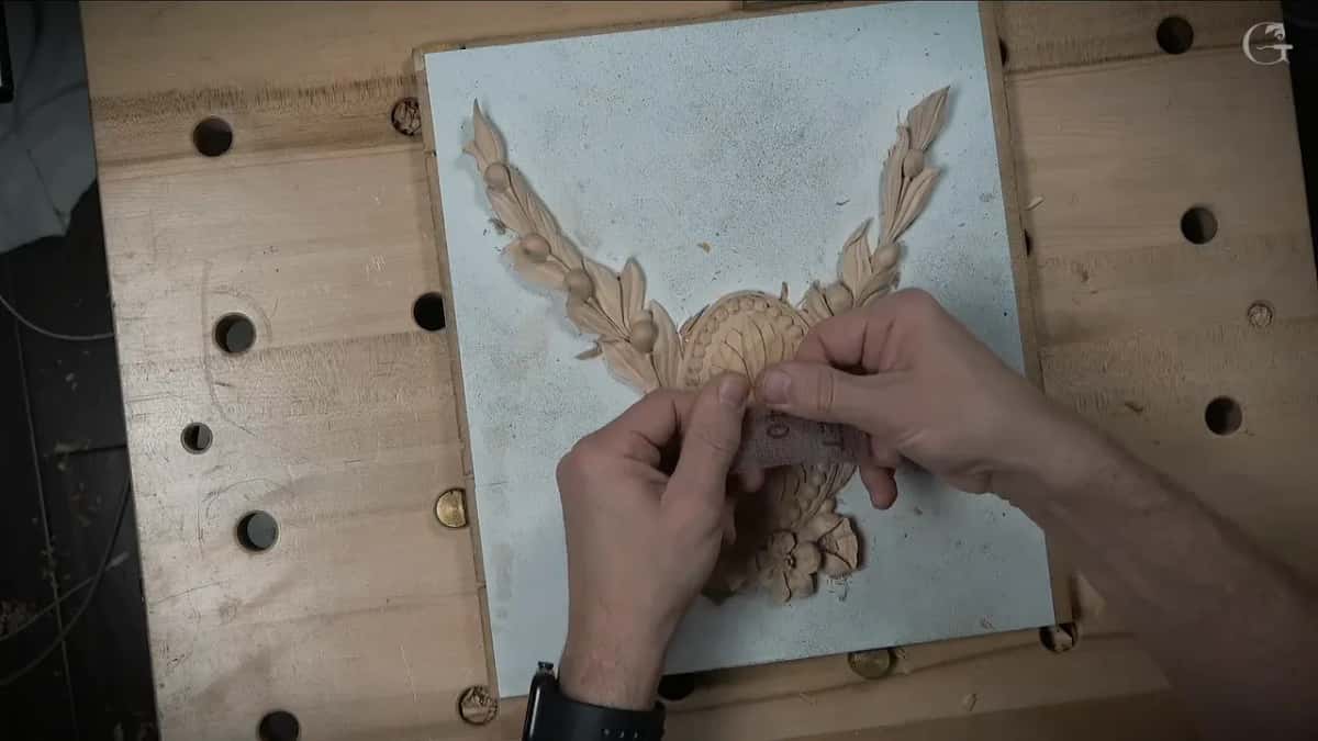 Two hands bend a strip of abrasive over the chamomile carving.