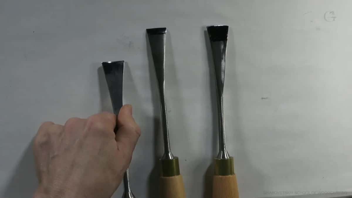 Three gouges stand in a row on a grey board, one hand gripping the first