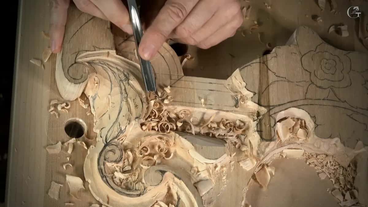 Pale curls of wood piled around the base of the leaf as the tool works its upper edge