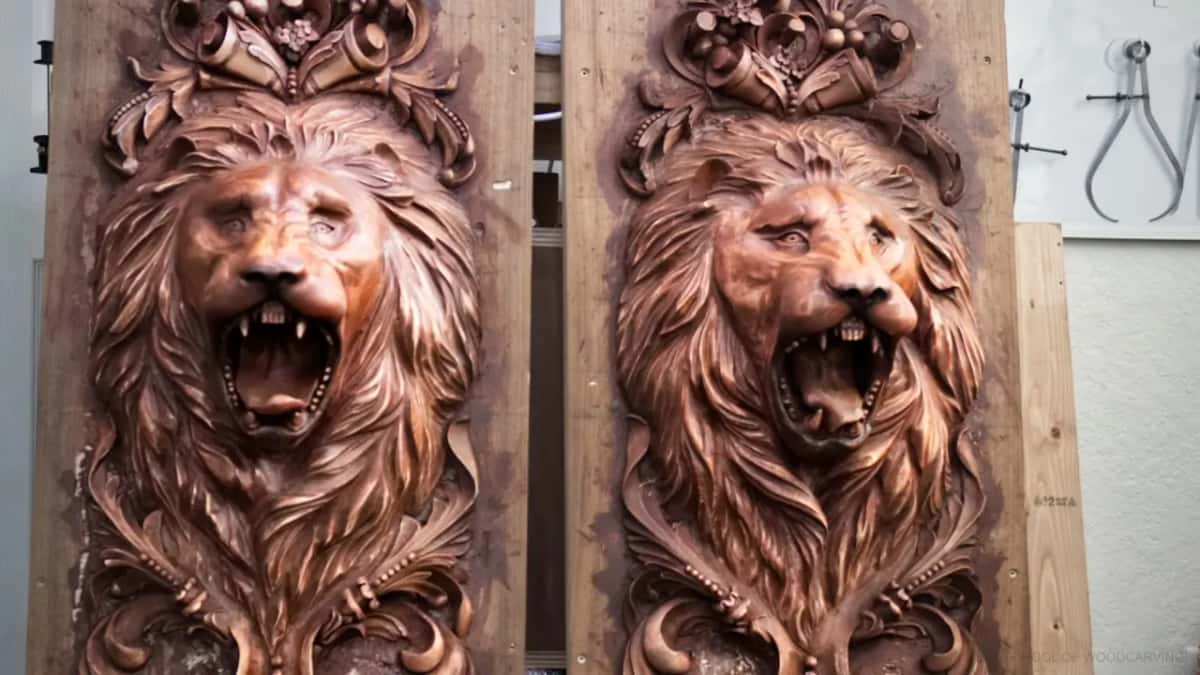Two lion heads with open mouths, carved in dark wood on tall boards
