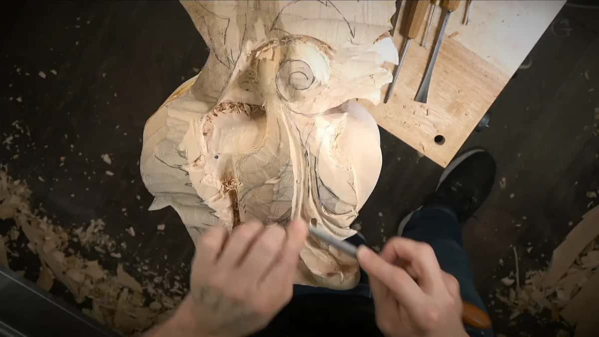 Both hands work a tool across the carving, seen from overhead