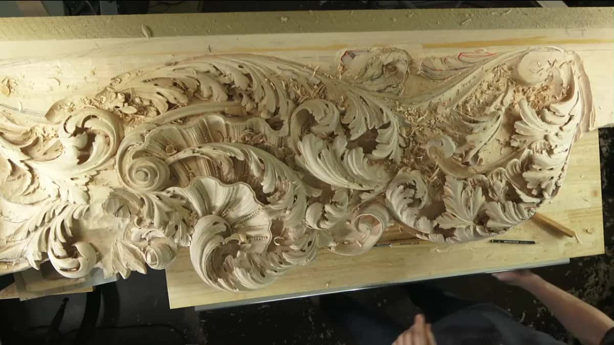 A long carved panel of leaves and scrolls seen from above, pencils lying on the bench below it